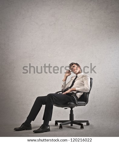 Young businessman calling lying on a chair