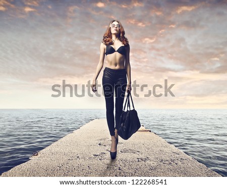 Beautiful girl in pants and bra walking on a pier