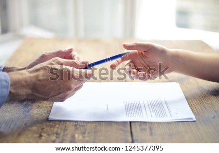 Hands giving a pen to an other hand above a desk.