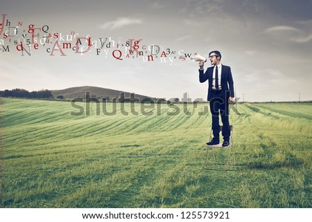 Businessman standing on a large field using a megaphone from which comes out colored words