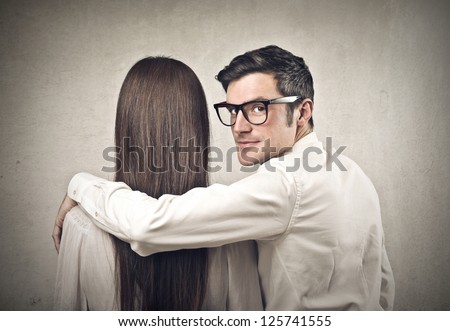 A man holds his arm on the shoulders of a woman and look at the lens behind them