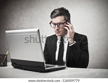 Serious businessman calling someone with a mobile phone while is using a laptop