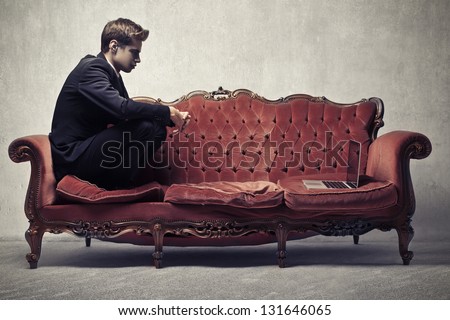young businessman sitting on red sofa with laptop