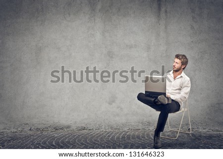 young businessman sitting on the chair with laptop on gray background young businessman sitting on the chair with laptop on gray background