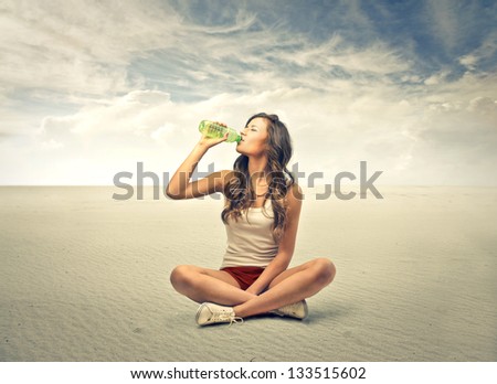 young girl sitting cross-legged drinking water from bottle in the desert