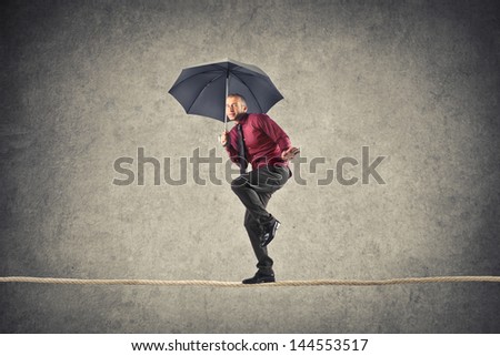 young businessman walking with umbrella balancing on rope