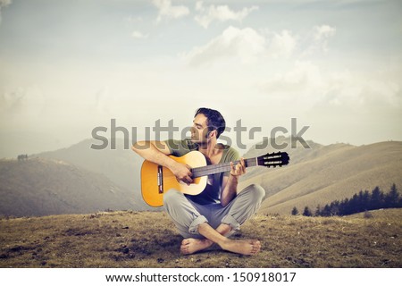 young guy playing guitar sitting on the grass