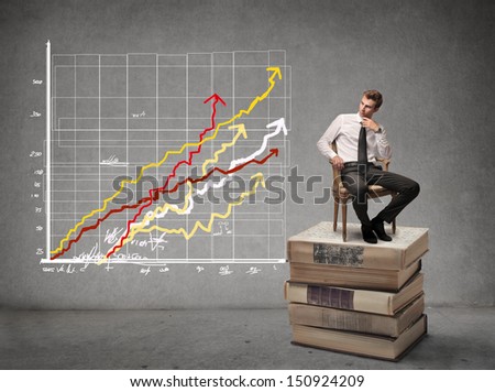 business man sitting on stack of books looks chart