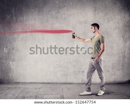 young boy painting on the wall with red spray