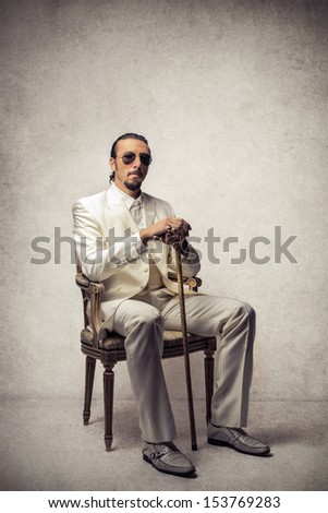 boss sitting on a chair dressed in white suit with stick and sunglasses