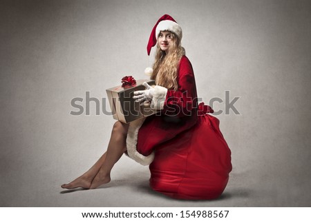 beautiful blonde woman with a big present dressed with Santa Claus clothes and sitting on a big red sack of gifts