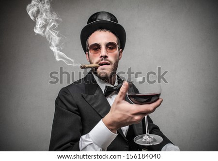 Elegant Man With Cylinder Smokes A Cigar And Drinks Red Wine