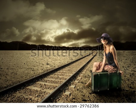 girl sitting on a suitcase along the  train tracks