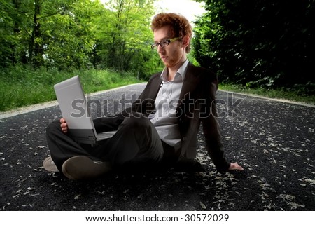 young man in formal suit using laptop on a country road