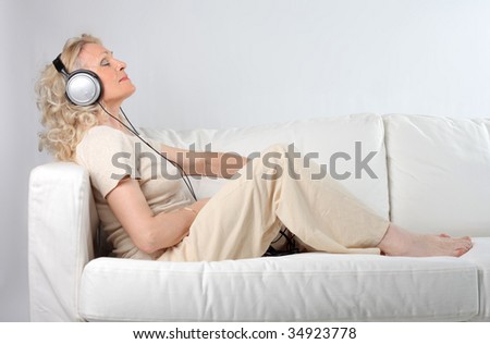 senior woman listening music with headphones on the sofa
