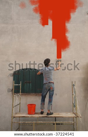 rear view of man painting in red colour an external wall