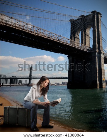 girl seated on suitcase reading book and bridge of brooklyn on the background