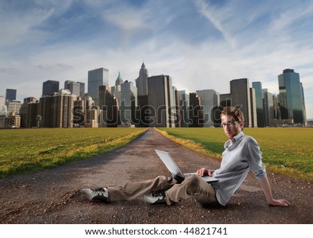 student working with laptop on a country road and modern city on the background