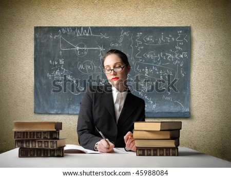 Portrait of a teacher sitting in front of a blackboard and writing on an exercise book