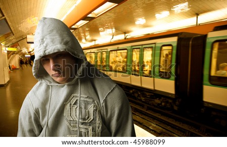 Portrait of a young man with his face covered by the hood of his sweatshirt standing on the platform of an underground station