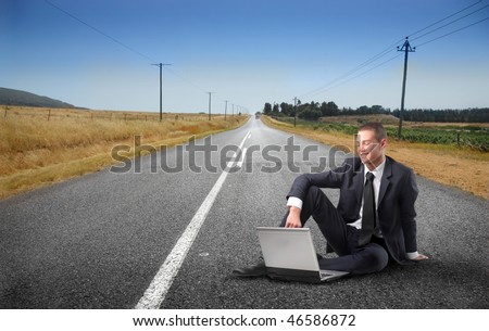 Portrait of a smiling young businessman sitting on a countryside road and using a laptop