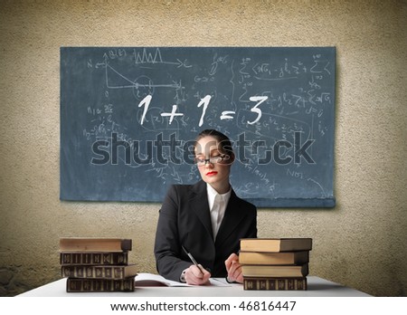 Portrait of a school teacher sitting at a desk with a blackboard with a wrong addition on it