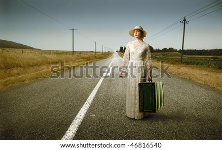 Portrait of an elegant woman standing on a countryside street with a suitcase in her hands