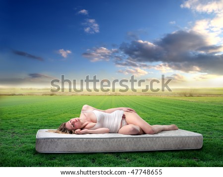 Portrait of a woman lying on a mattress on a green field