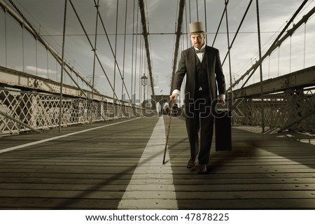 Portrait of an elegant man crossing a bridge with an old suitcase in his hand