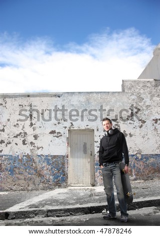 Portrait of a young man in street wear standing in front of an ancient building with a skateboard in his hand