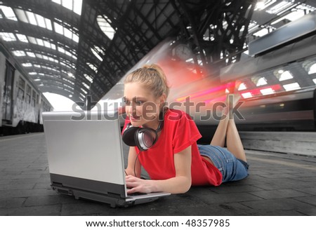 Young woman lying on the platform of a train station with a laptop in front of her