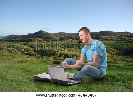 Smiling young man sitting on a green meadow with a laptop in front of him