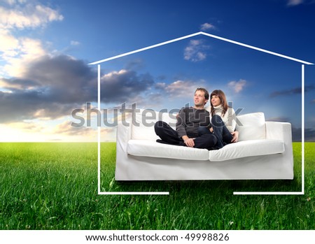 Young couple sitting on a couch on a green meadow surrounded by the form of a house
