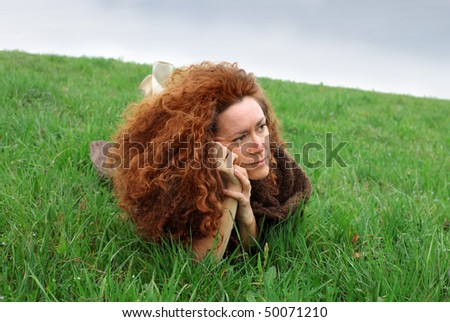 Red haired woman lying on a green meadow with sad expression