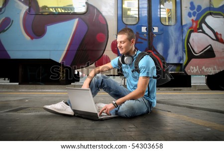 Young man sitting on the platform of a train station and using a laptop
