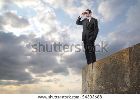 Businessman standing on a rock and using binoculars