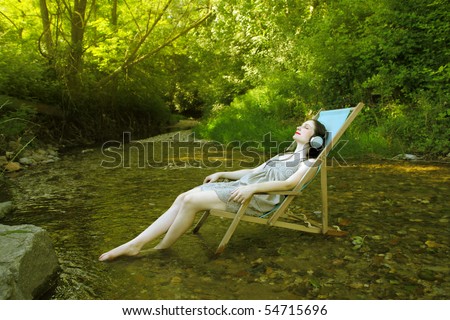 Woman lying on a deckchair in a stream and listening to music