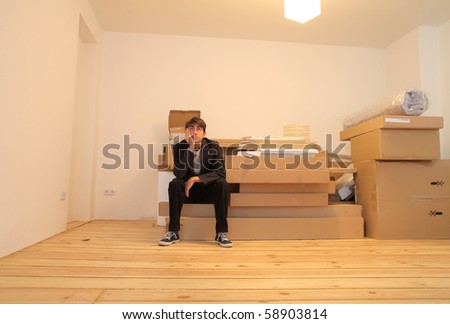 Young man sitting on a pile of furniture packing in an empty flat