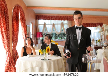 Young waiter in a restaurant with couple on the background