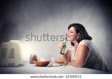 Fat woman sitting in front of the television and drinking a beer