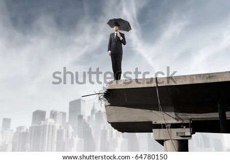 Businessman with umbrella standing on the edge of a broken bridge