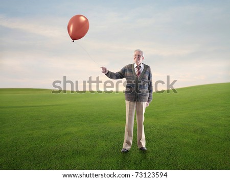 Smiling senior man holding a balloon on a green meadow