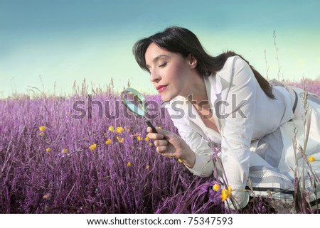 Woman observing some flowers through a magnifying glass