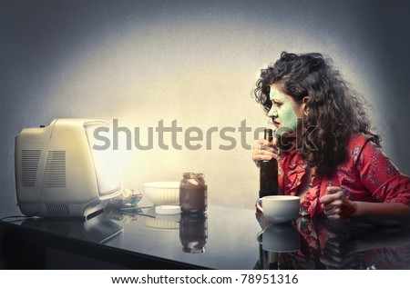 Woman wearing face mask sitting in front of the television and drinking beer