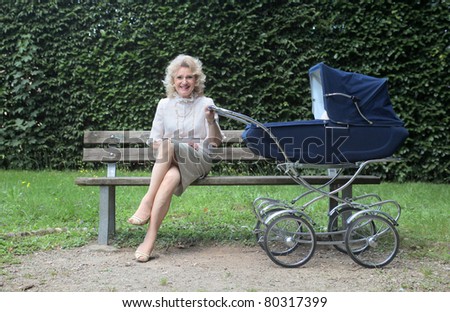 Smiling grandmother sitting on a park bench and holding the handle of a pram