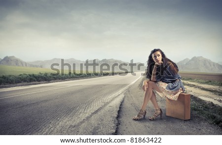 Beautiful woman sitting on a suitcase by a countryside road