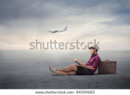 Young man sitting against a suitcase with airplane in the background