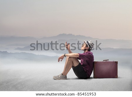 Tourist sitting against a suitcase in a desert and using a mobile phone