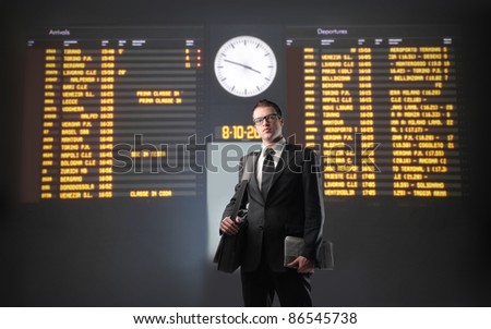 Businessman with departures and arrivals board of a train station in the background