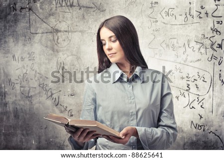 Beautiful woman reading a book with calculations on the blackboard in the background